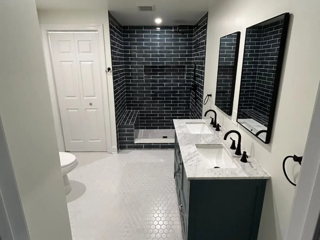 Remodeled bathroom in Berwyn, PA with white honeycomb floor tile, black tiled shower, double vanity and new mirrors.