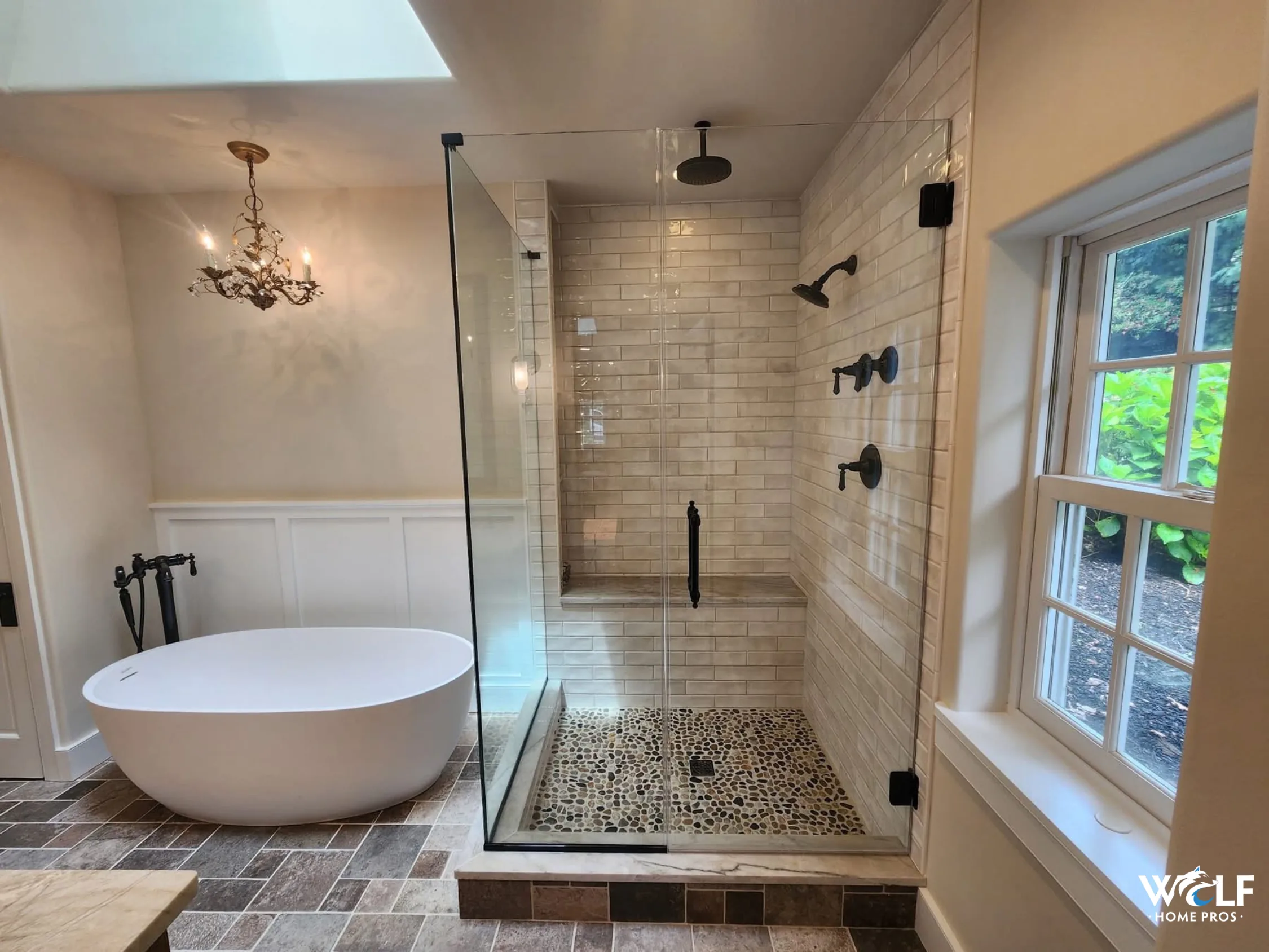 Bathroom remodel in Berwyn, PA with a tiled walk-in shower, freestanding soaking tub, black fixtures and tile flooring.