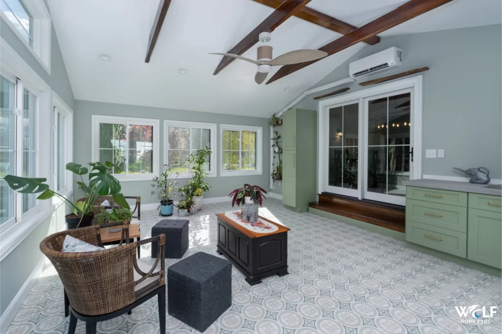 Finished Coatesville sunroom with exposed wood beams, patterned tile floor, green cabinetry, and glass doors.
