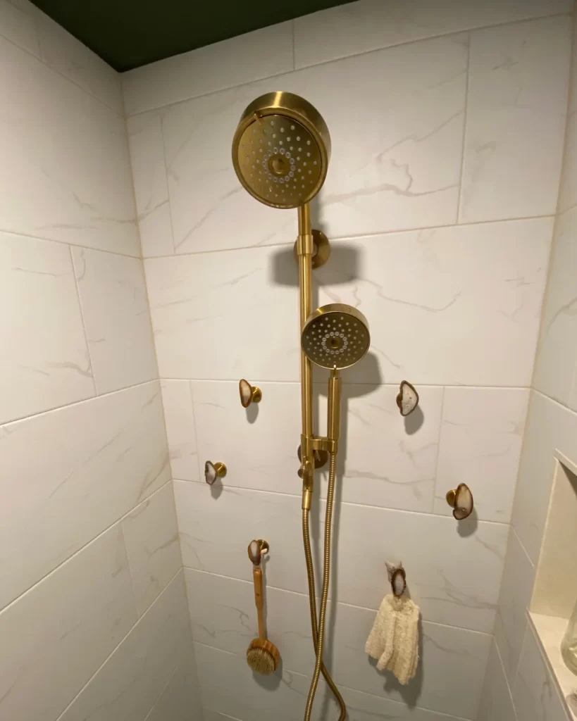 Close-up of shower fixtures and wall hooks in a Downingtown, PA bathroom remodel with marble-look tile.