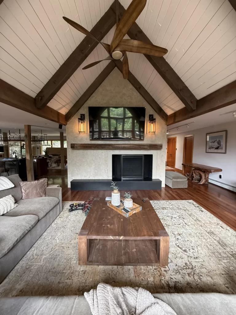 Downingtown, PA living room with a custom microcement fireplace wall, reclaimed wood mantel and exposed ceiling beams.