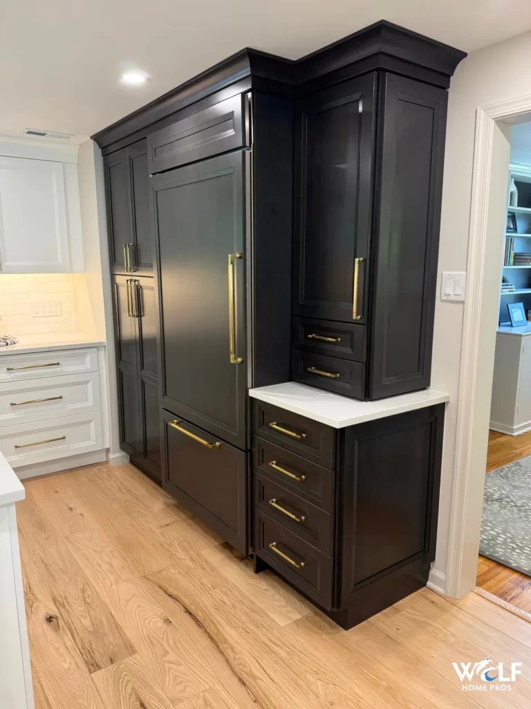 Custom kitchen cabinetry in Gladwyne, PA by Wolf Home Pros featuring a paneled refrigerator surround, dark built-ins, and brass hardware.