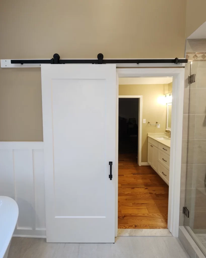 Custom white sliding door with black track hardware, wall paneling and finished trim in a West Chester, PA bathroom remodel.
