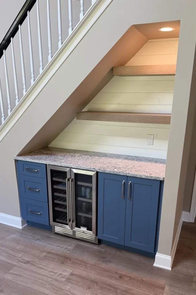 Custom under-stair wet bar with blue cabinetry, floating shelves, lighting and beverage refrigerator in Downingtown, PA.