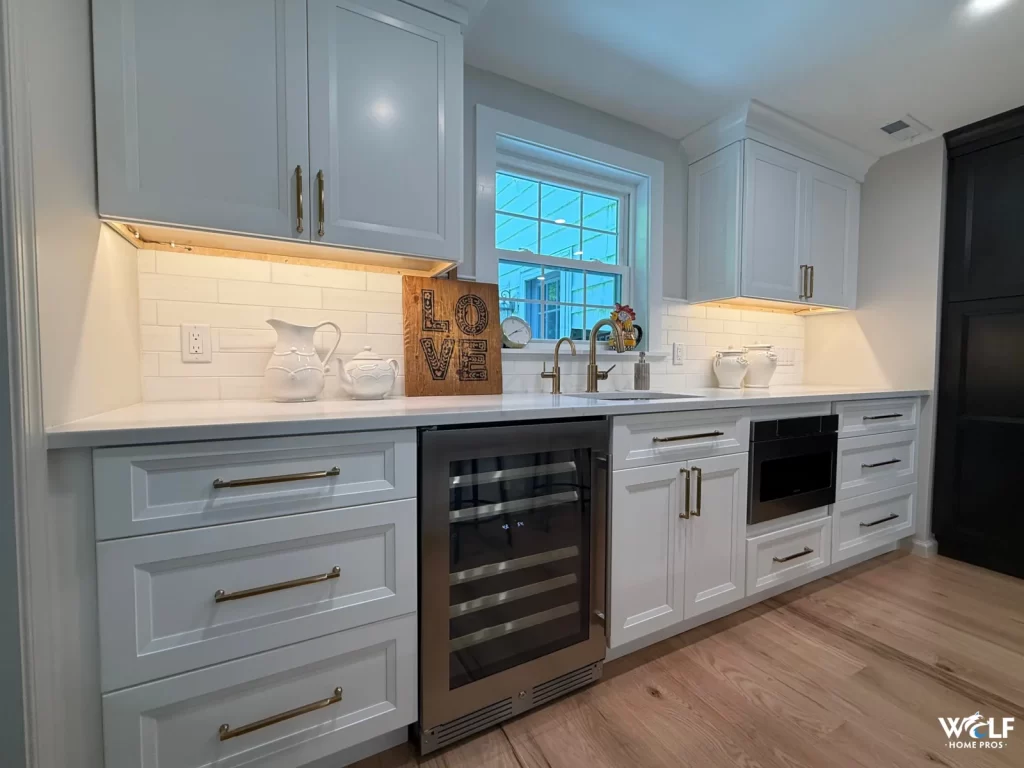 Custom wet bar area in Gladwyne, PA by Wolf Home Pros featuring built-ins, a beverage refrigerator, sink, microwave drawer, and under-cabinet lighting.
