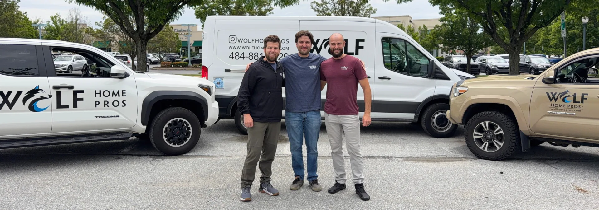 Dan, Phil, and James Wolf standing together between Wolf Home Pros work vehicles.