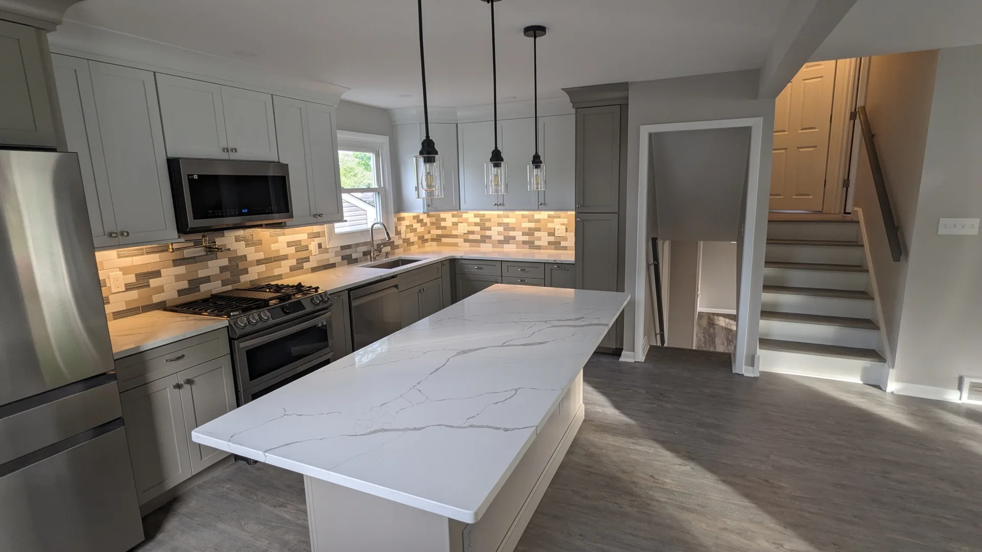 Finished kitchen remodel in Phoenixville, PA with new cabinetry, island, countertops, appliances, backsplash, and hardwood flooring by Wolf Home Pros.