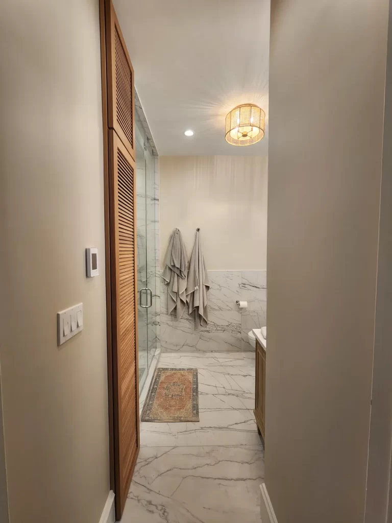 Entry view of a remodeled bathroom in Villanova, PA with tiled flooring, glass shower, updated lighting, and wood louvered doors.