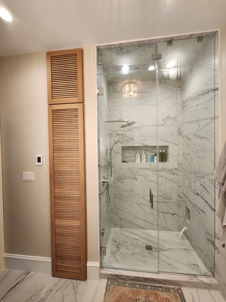 Glass-enclosed walk-in shower in a Villanova, PA bathroom remodel with large-format tile, rainfall showerhead, handheld fixture, and recessed niche.