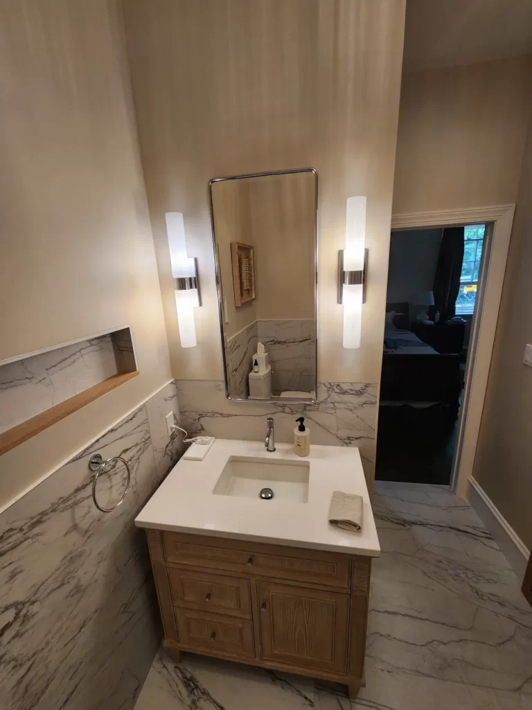 Bathroom vanity in Villanova, PA with wood cabinetry, white countertop, wall tile, mirror, and updated sconce lighting.