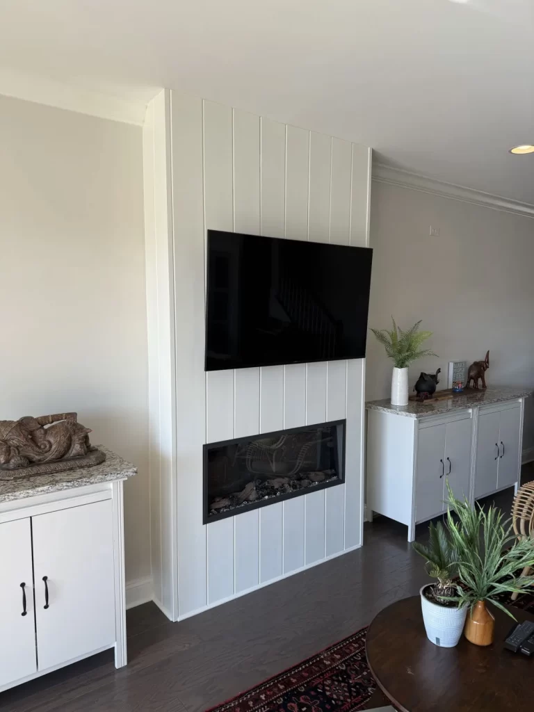Fireplace installation in Wayne, PA with a modern white surround, wall-mounted television, and built-in cabinetry.