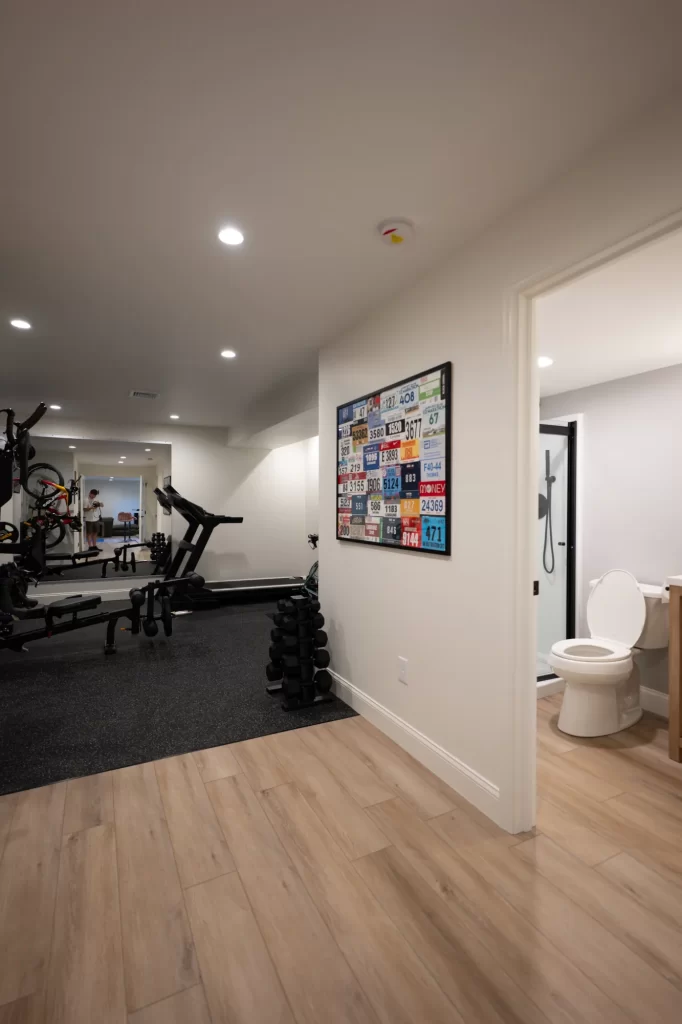 Finished West Chester basement with home gym, rubber flooring, recessed lighting, and adjoining bathroom entrance.