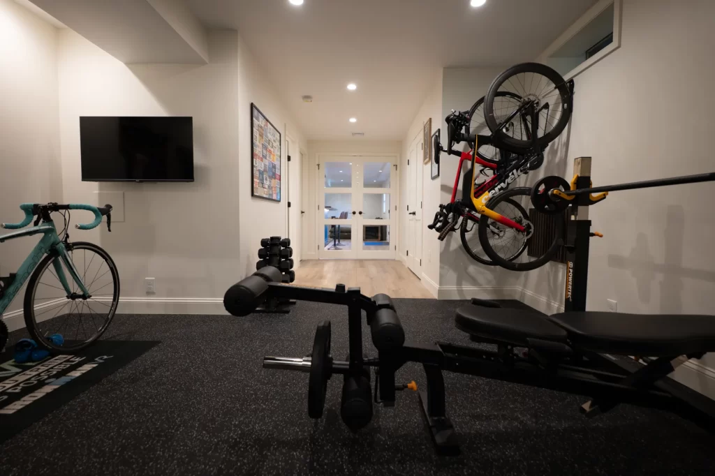 West Chester basement home gym looking toward the main finished basement with bike storage, workout equipment, television, and glass doors.