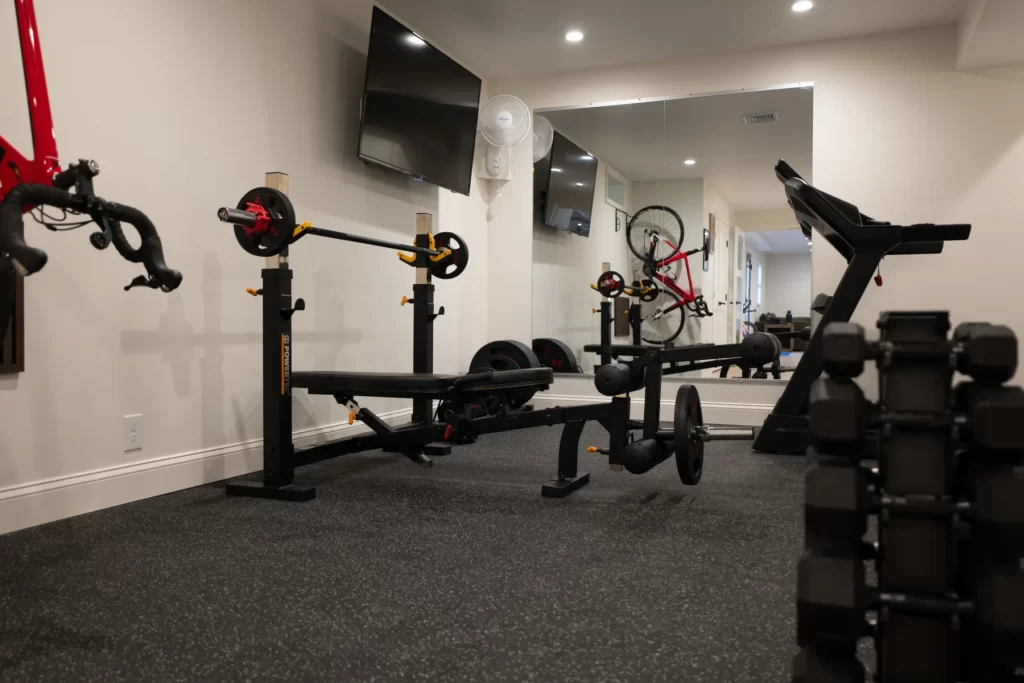 Finished basement home gym in West Chester, PA with rubber flooring, wall mirror, mounted television, workout equipment, and bike storage.