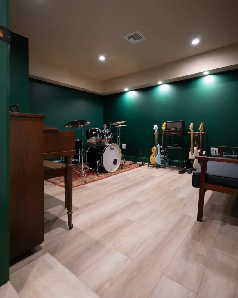 Finished basement music room in West Chester, PA with drum set, piano, guitars, wood flooring, green walls, and recessed lighting.