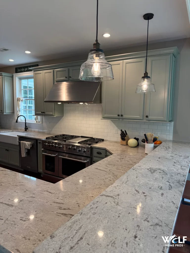 Finished kitchen backsplash project in West Chester, PA with white tile, green cabinetry, stone countertops, and stainless range hood.