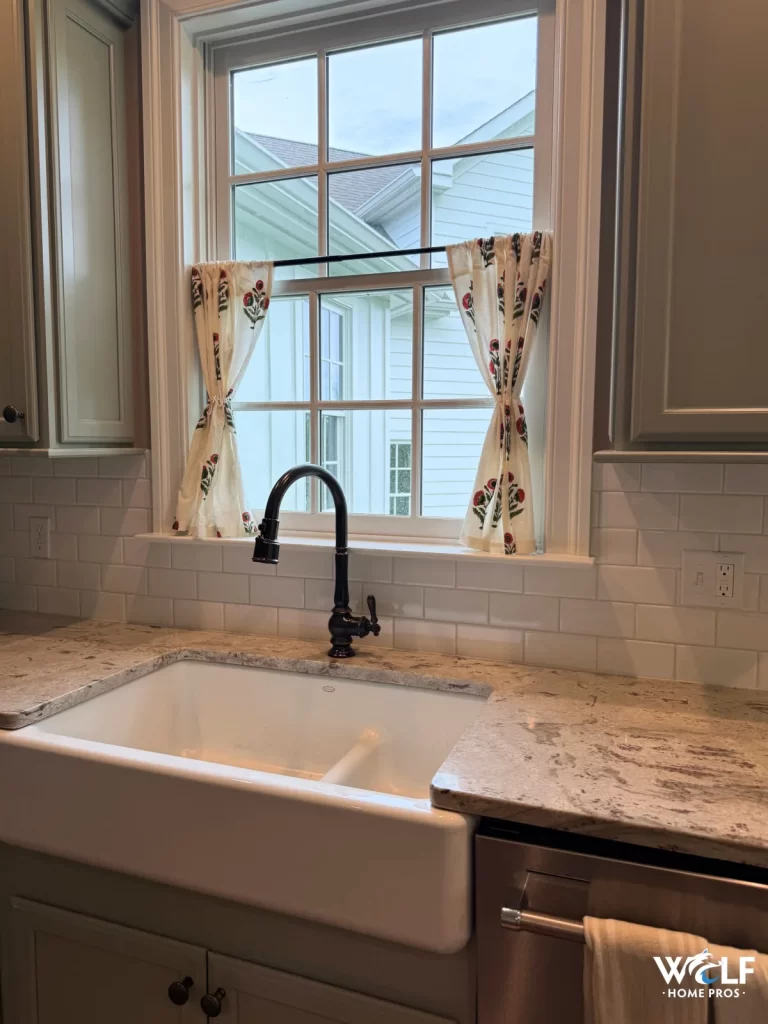 Finished kitchen sink area in West Chester, PA with white tile backsplash, farmhouse sink, stone countertop, and black faucet.